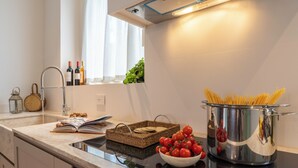 Una cocina moderna con una olla de acero inoxidable llena de espagueti, un tazón de tomates y un libro sobre la encimera.