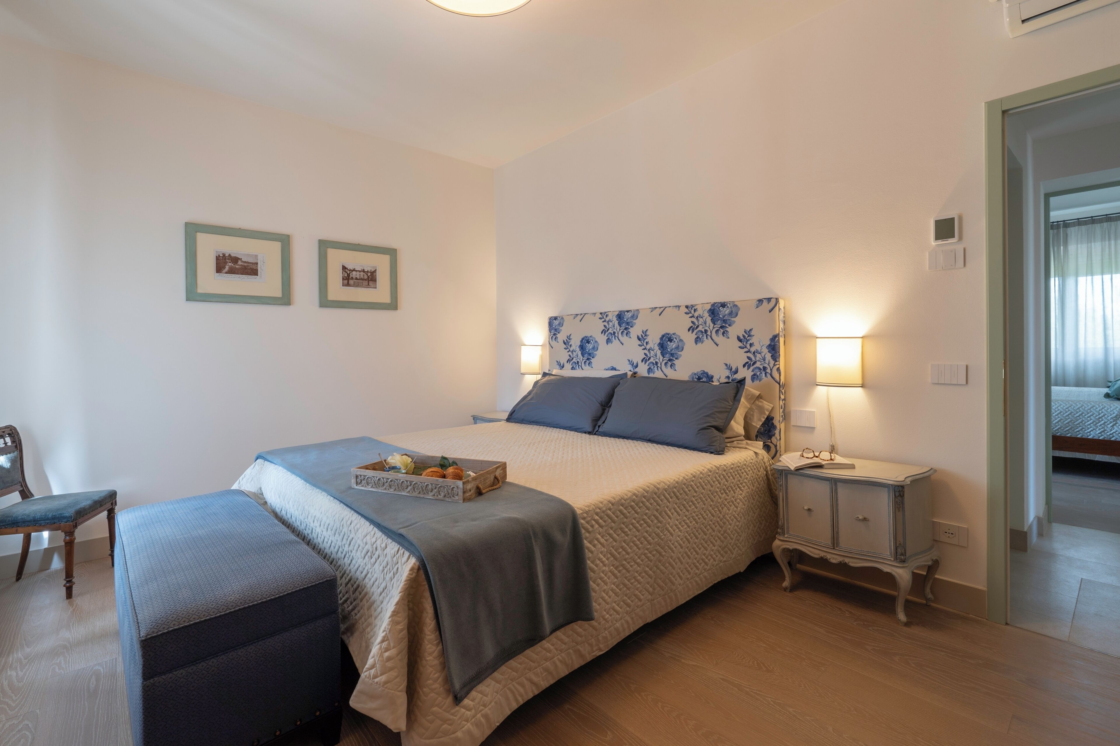 Een slaapkamer met een bed, nachtkastje, lamp en een stoel.