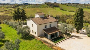 Una casa moderna con techo de tejas, rodeada de olivares y campos abiertos.