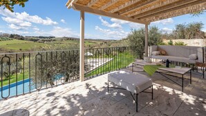 Zona de estar al aire libre con techo y vistas a una piscina y al campo.