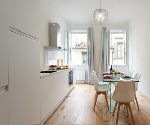 Una cucina moderna con mobili bianchi, un'area pranzo con tavolo in vetro e vista all'esterno tramite ampie finestre.