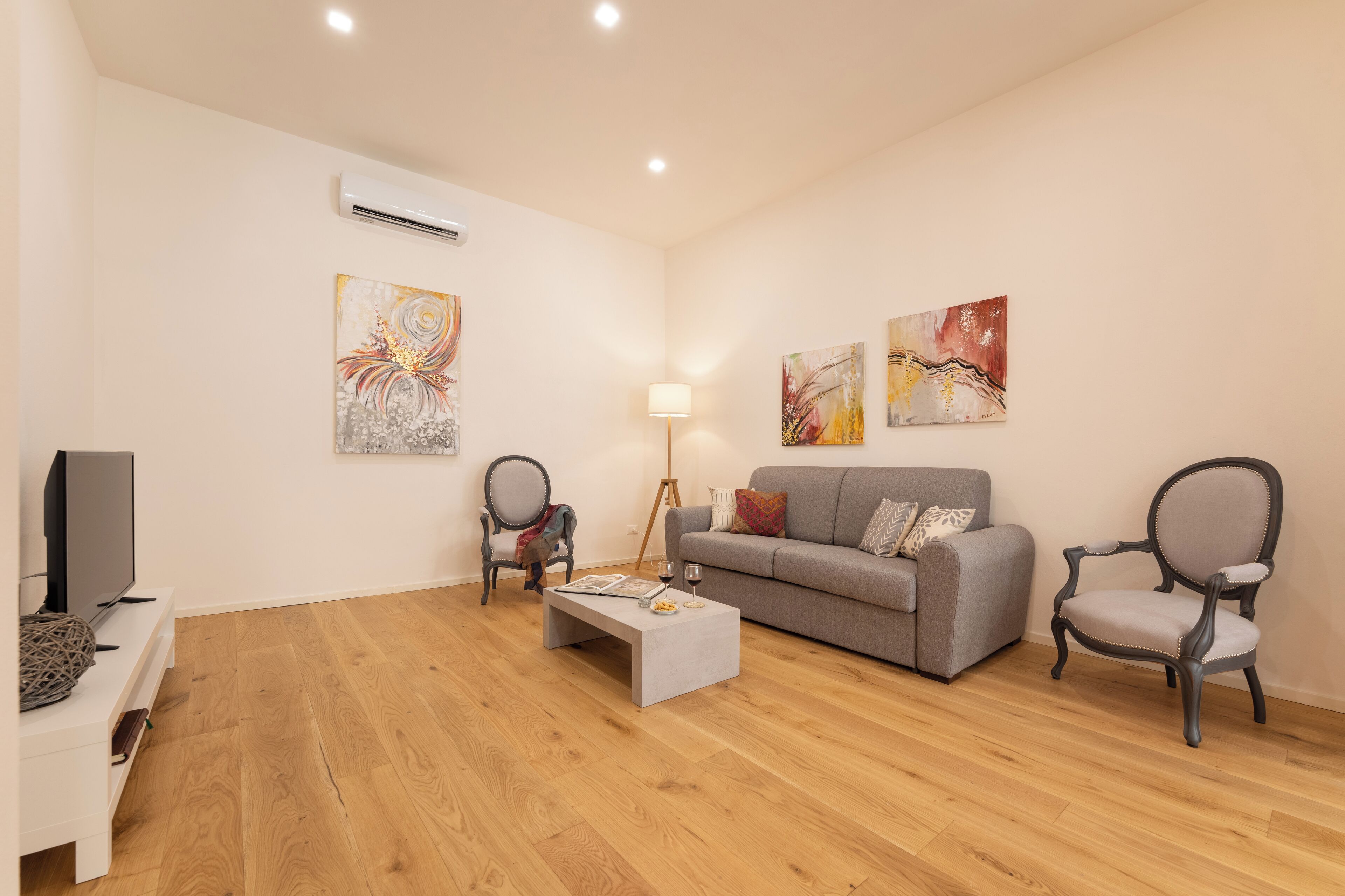 Un salon moderne avec un canapé gris, deux fauteuils, une table basse et des œuvres d’art accrochées aux murs.