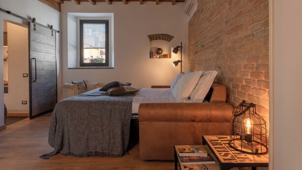 A cozy bedroom with a bed, a sofa, a table with a lamp, and a brick wall. - Santa Trinita - Flo Apartments (Florence)