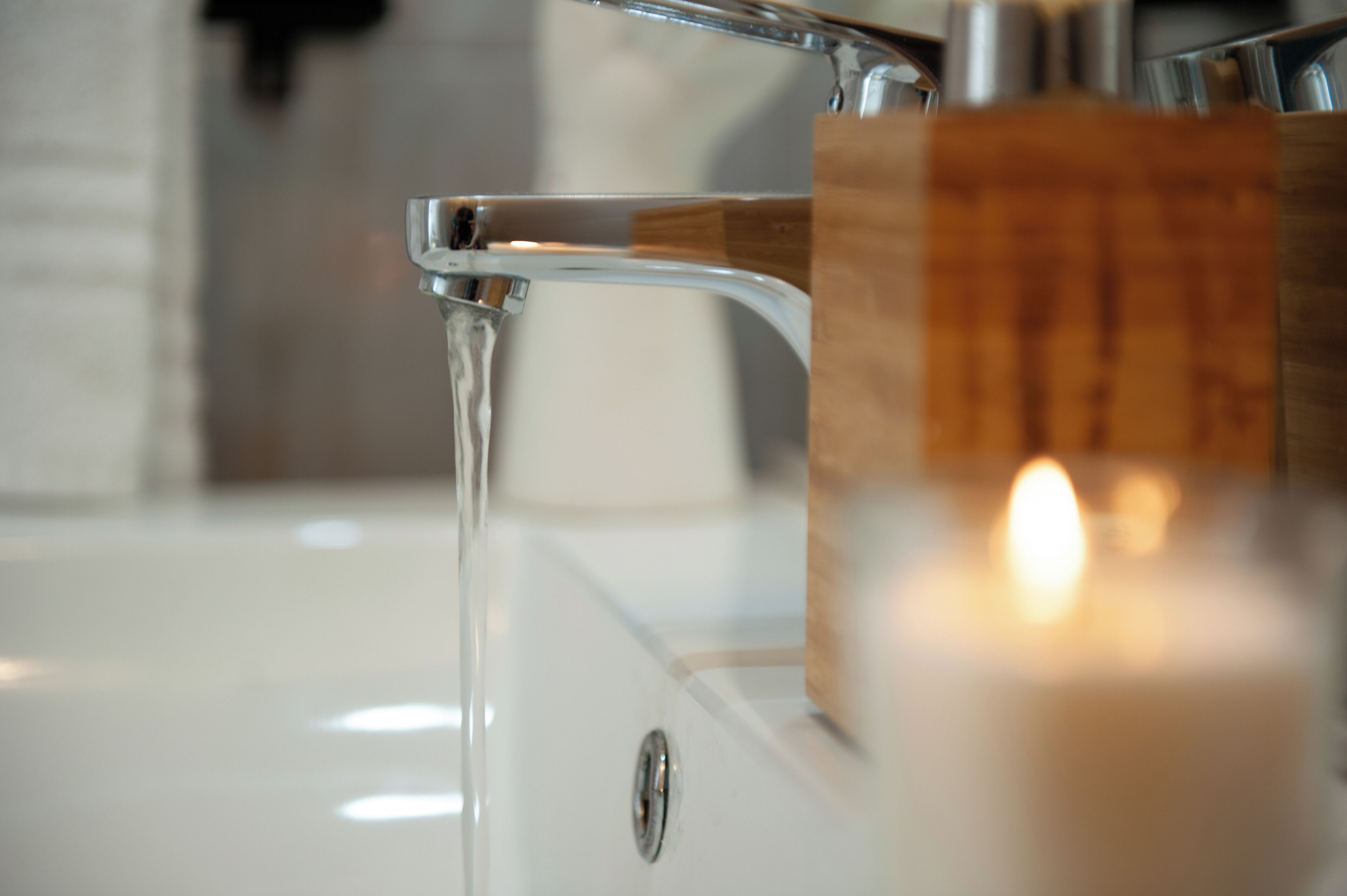 A bathroom sink with running water, a wooden soap holder, and a lit candle.