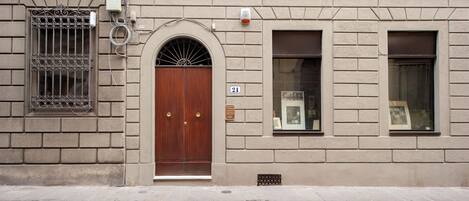 Un bâtiment avec une porte en bois, une fenêtre ornée d’un cadre et une plaque portant le numéro 21.