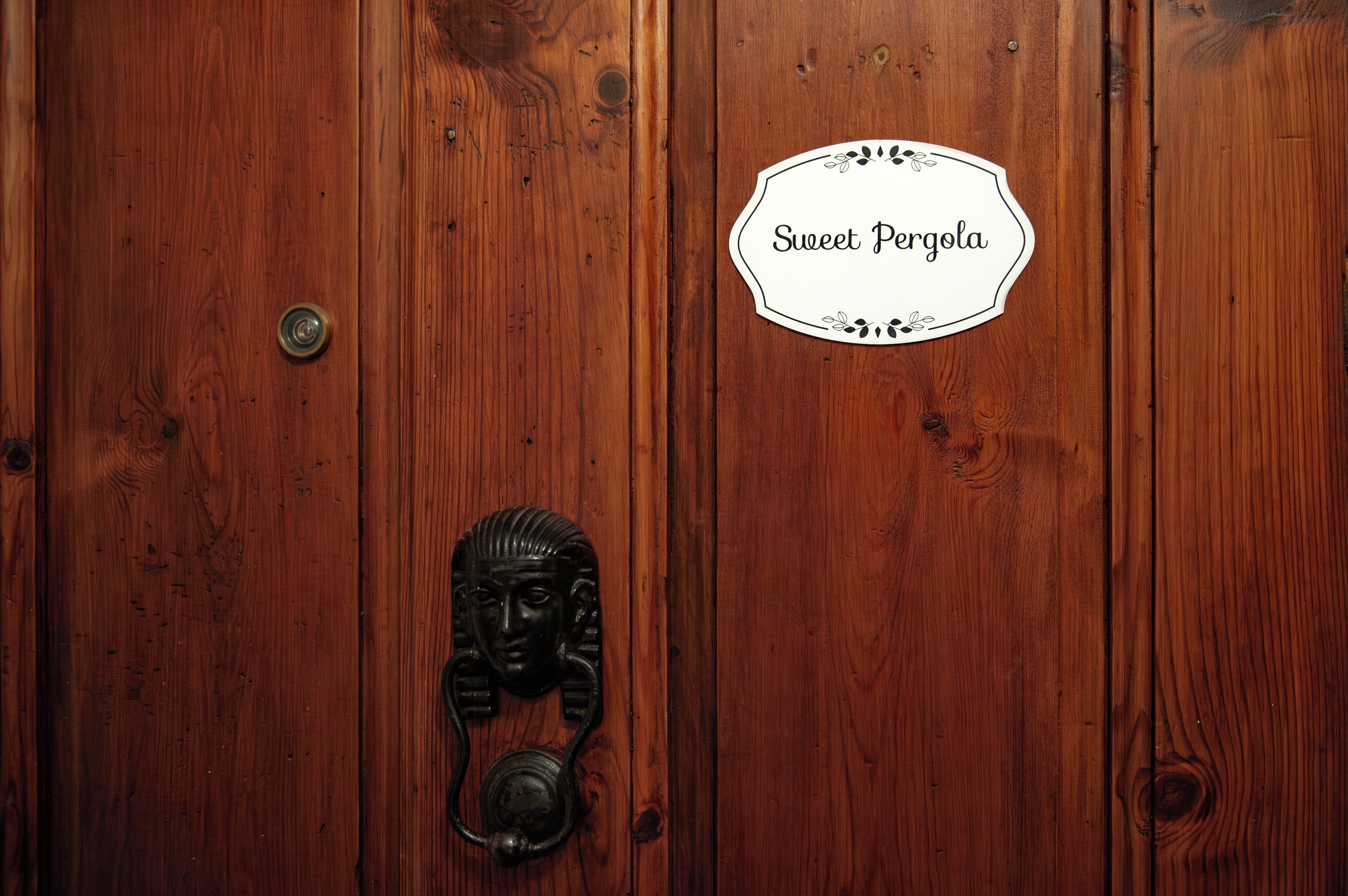 A wooden door with a metal handle and a sign that reads "Sweet Pergola."