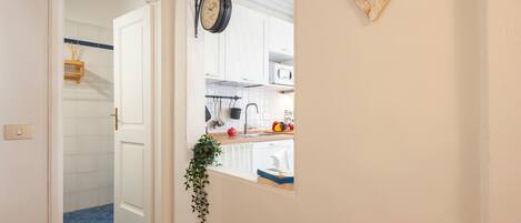 A hallway leading to a kitchen with a white door, a hanging clock, and a heart-shaped decoration.