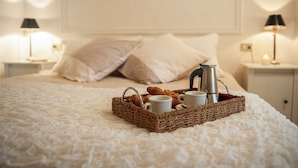 Un letto rifatto con cura, un vassoio con croissant, due tazze di caffè e un teiera su una coperta bianca con trama.
