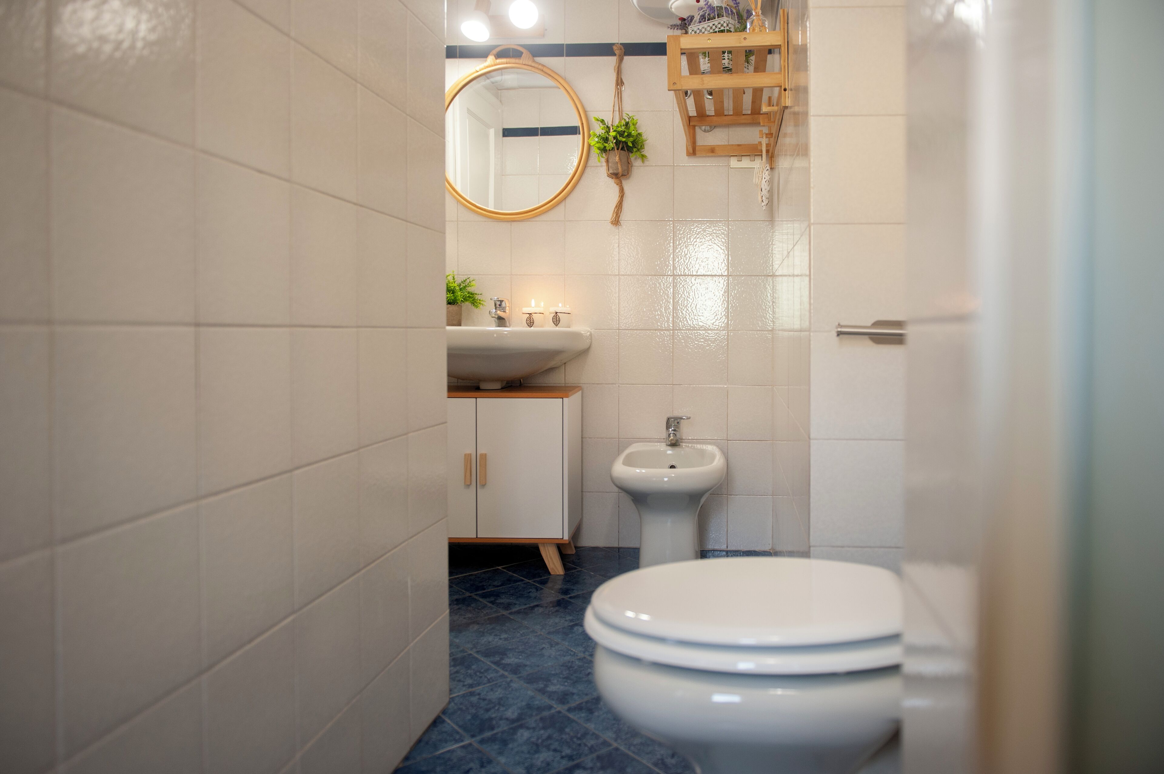 Une salle de bain avec un lavabo blanc, un miroir rond, un bidet et des toilettes.