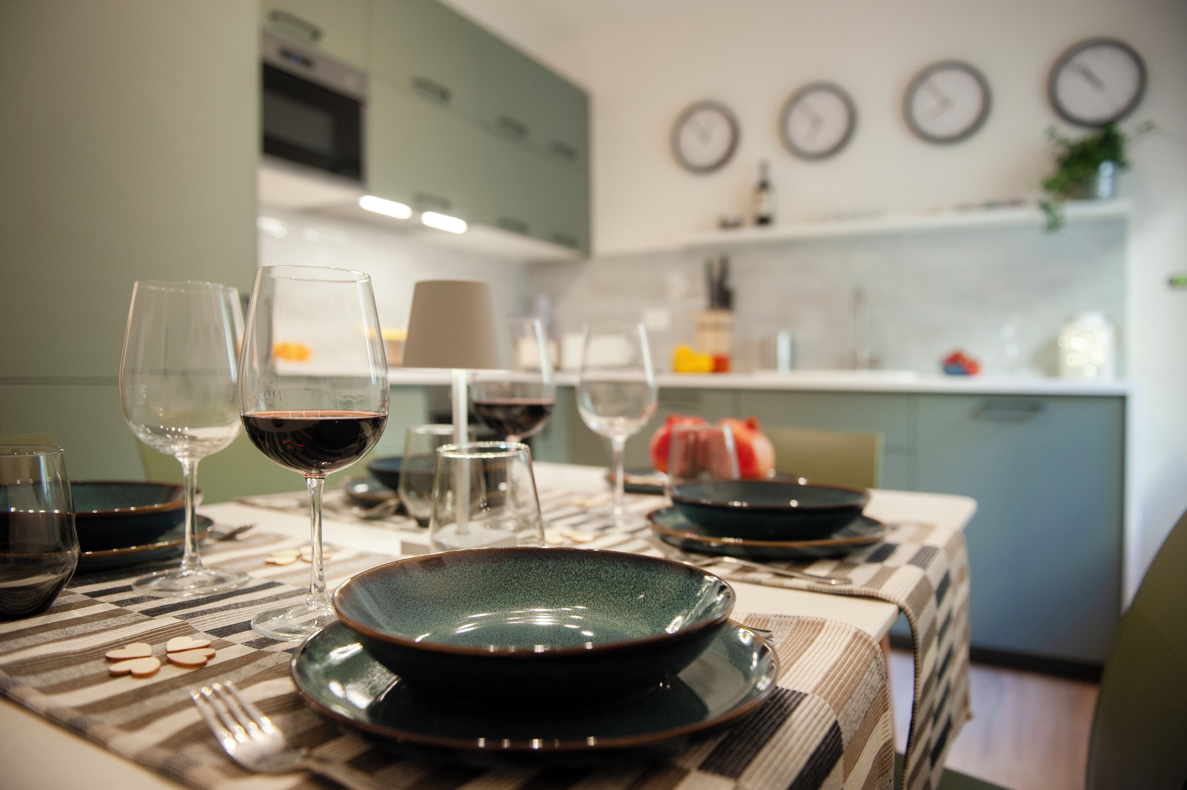 Una mesa de comedor dispuesta con platos, vasos y cubiertos en una cocina moderna con un reloj en la pared.