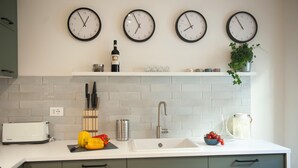 A kitchen with four wall clocks, a toaster, a sink, and a shelf with a bottle and a plant. - Canto Rivolto - Flo Apartments (Florence)