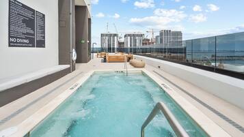 Una piscina en la azotea con vistas despejadas al horizonte urbano y grúas de construcción al fondo.