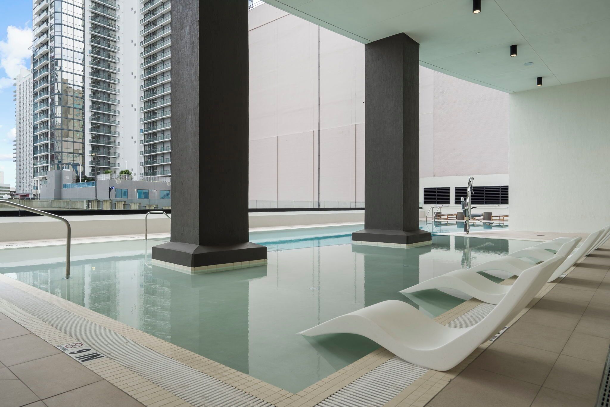 Een modern binnenzwembad met helder water, omringd door hoge gebouwen en uitgevoerd in een minimalistisch design met witte ligbedden.