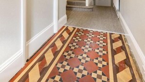 Un couloir avec un sol à motifs, un escalier et un miroir au mur.