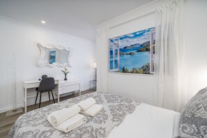 A hotel room with a bed, a desk, a chair, a mirror, and a window with a view of a body of water. - Studio 'Casa Onze' with Sea View, Wi-Fi and Air Conditioning (Portimão)