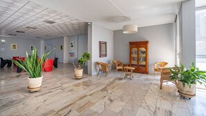 Tilava aula, jossa on marmorilattia, rottinkihuonekaluja, ruukkukasveja ja puinen kirjahylly.