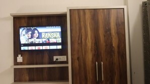 Μια τηλεόραση είναι τοποθετημένη σε έναν ξύλινο τοίχο, με ένα ράφι από κάτω όπου εκτίθενται διάφορα εικονίδια.