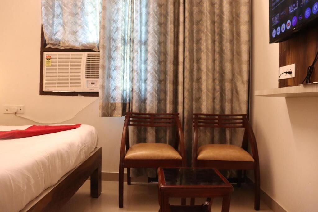 Een hotelkamer met een bed, twee houten stoelen, een tafeltje, een televisie en een airconditioner.