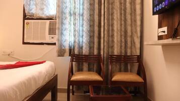 Een hotelkamer met een bed, twee houten stoelen, een tafeltje, een televisie en een airconditioner.