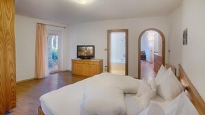 Een slaapkamer met een groot bed, een televisie op een houten dressoir en uitzicht buiten via een deur.