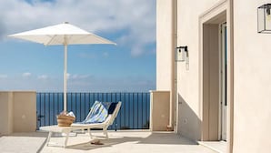 Un balcón con una sombrilla blanca, una silla de lounge y una cesta de mimbre.