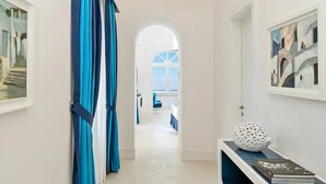 Un pasillo con vista a una sala de estar, que incluye una cortina azul, un objeto esférico blanco y un cuadro en la pared.