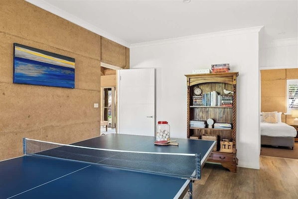 A ping pong table in a room with a bookshelf, a door, and a bed.