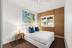 A bedroom with a bed, a nightstand, a lamp, a window, and a painting on the wall.