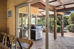 An outdoor patio with a barbecue grill, a covered seating area, and a view of the surrounding greenery. - Waterlily Retreat—Bushland Serenity near the Beach (Eagle Bay)