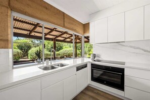 Una cocina moderna con armarios blancos, horno empotrado, fregadero y ventana con vista a follaje.