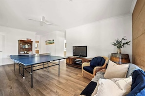 A living room with a ping pong table, a television, a bookshelf, and a wicker sofa.