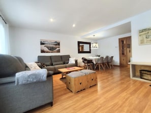 A living room with a sofa, a wooden coffee table, a dining table with chairs, and a fireplace. - Casa Arguis Country House with Mountain Views, Wi-Fi, and Air Conditioning (Eriste)