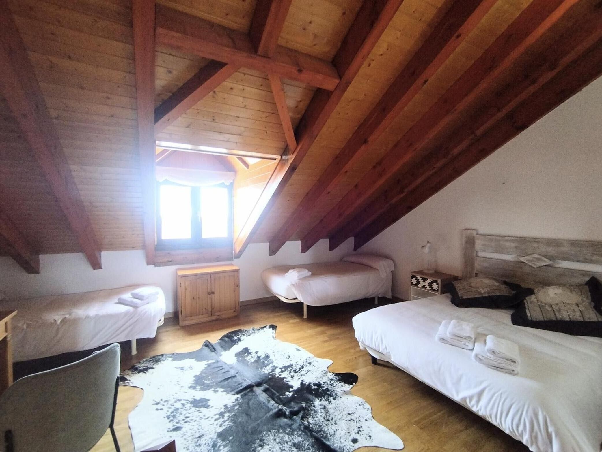 Une pièce avec un plafond en pente, des poutres apparentes, deux lits, une petite armoire et un tapis en peau de vache.