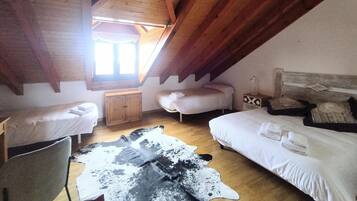Une pièce avec un plafond en pente, des poutres apparentes, deux lits, une petite armoire et un tapis en peau de vache.