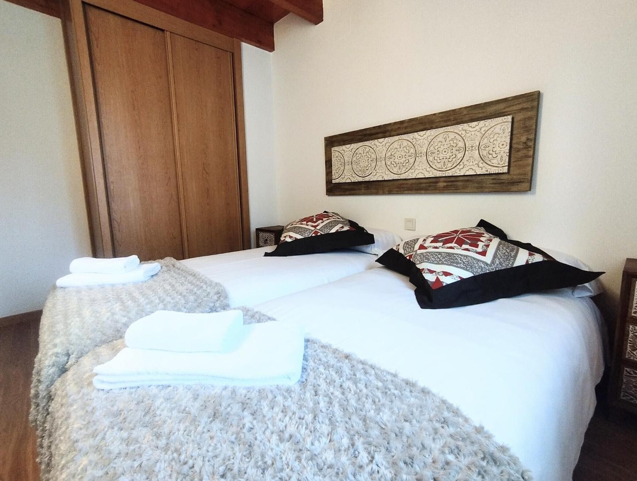 Una cama doble con almohadas estampadas, una toalla doblada y un adorno en la pared.