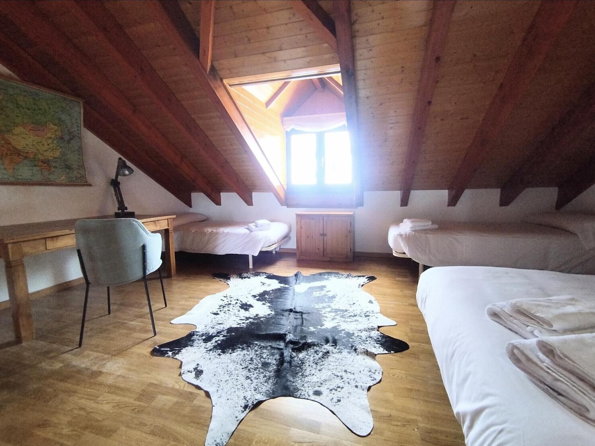Ein gemütliches Schlafzimmer unter dem Dach mit Holzbalken, einem Schreibtisch, zwei Betten und einem Cowhide-Teppich.