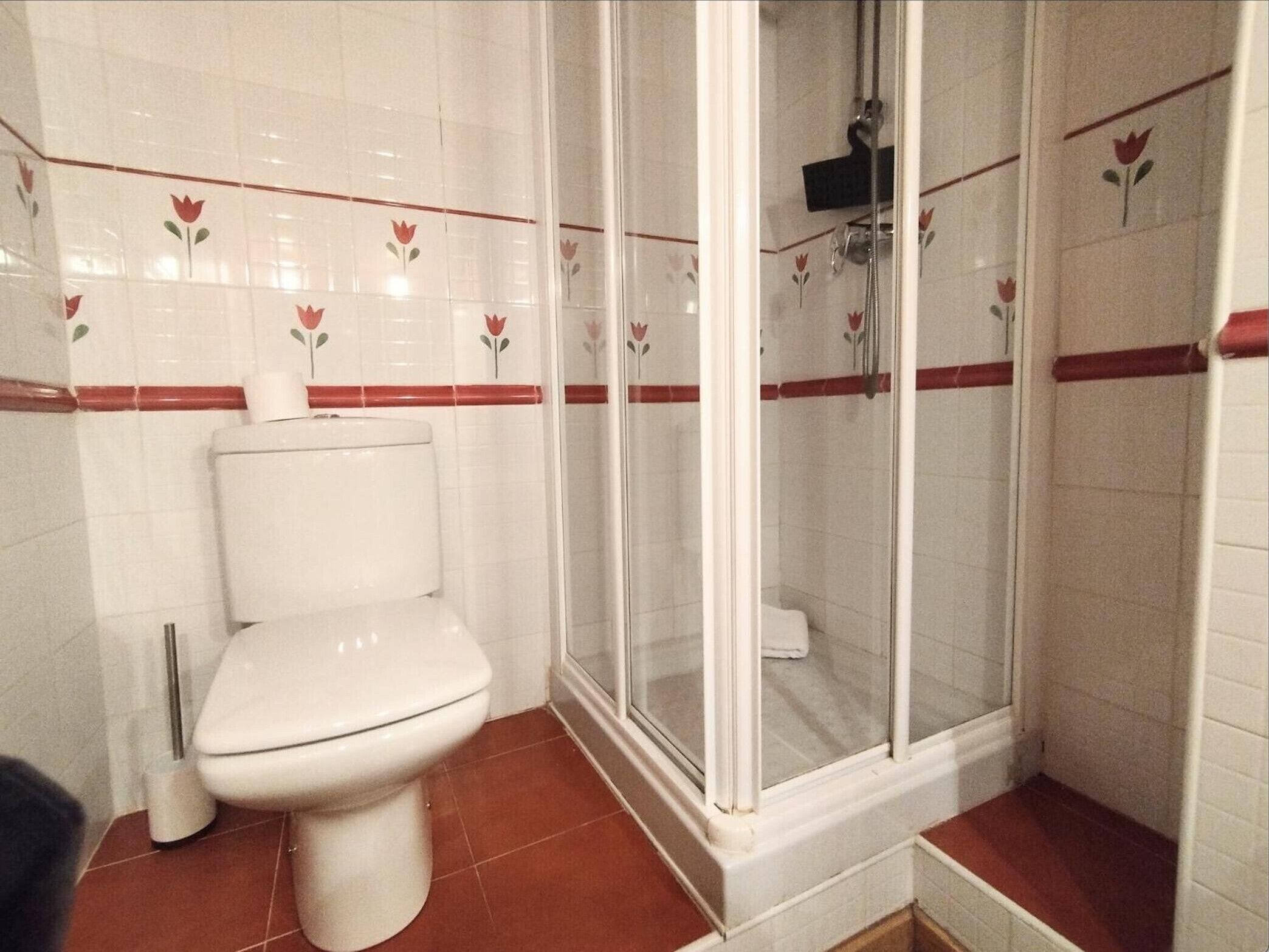 Un baño con inodoro, cabina de ducha y dispensador de papel higiénico.