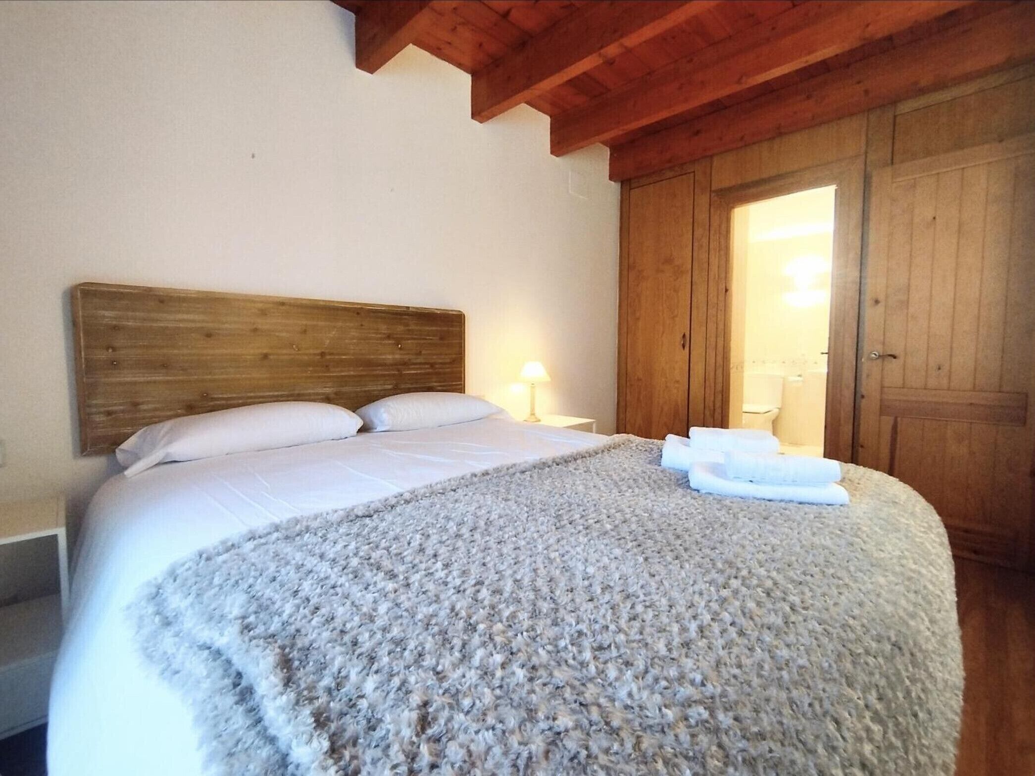 Ein Schlafzimmer mit einem hölzernen Kopfteil, einem großen Bett mit weißer Bettwäsche, einem flauschigen Teppich und einem Holzschrank.
