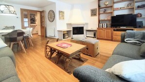 Uma sala de estar com uma mesa de madeira, um sofá, uma televisão e uma lareira.