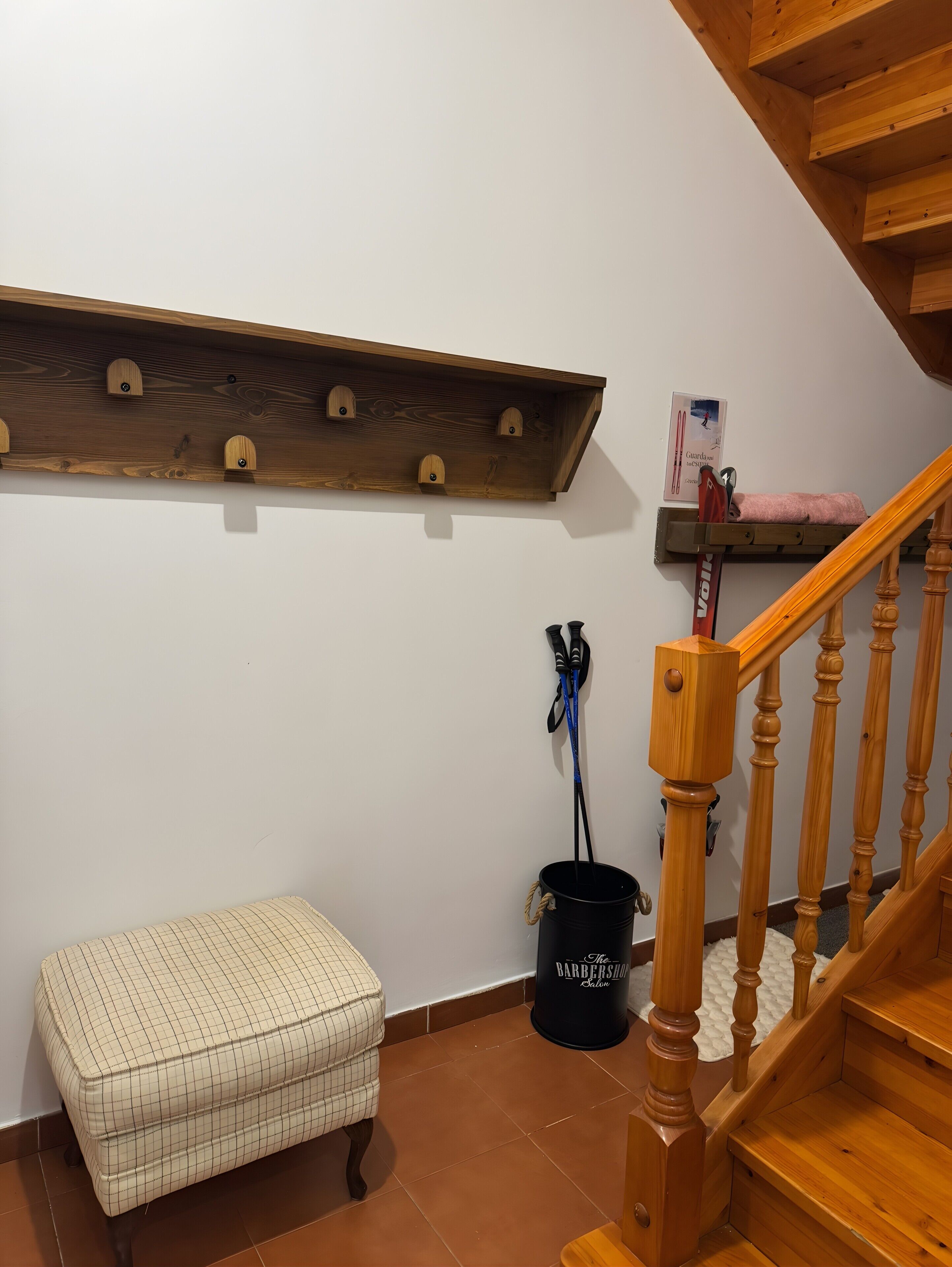 A staircase with wooden balusters, a bench, a shelf with hooks, and a bucket labeled 'The Barber Shop.'