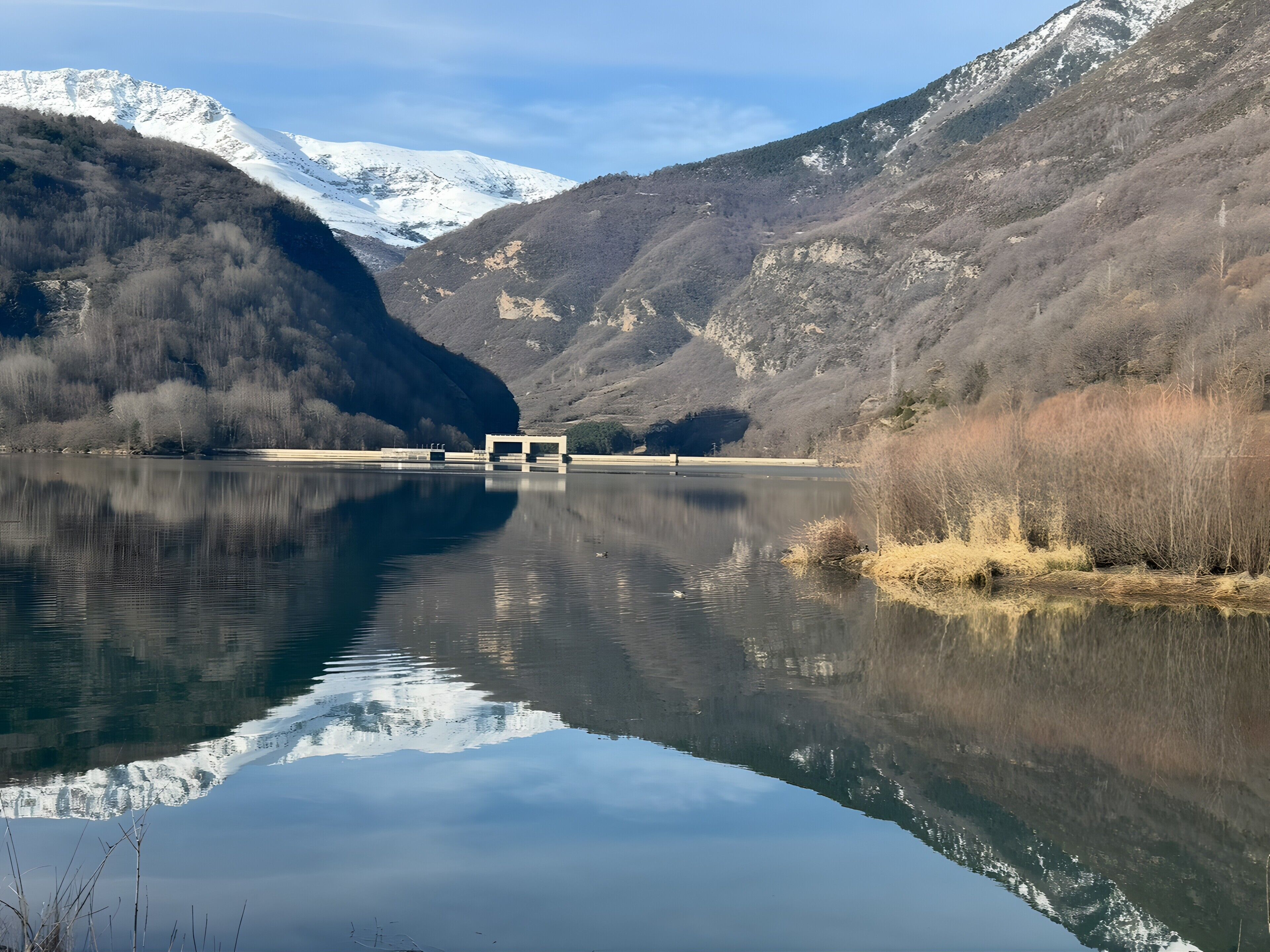 A tranquil lake with a mountain backdrop, a small building in the center, and clear skies.