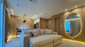 Un salon moderne avec un canapé, un coin cuisine à l’arrière-plan et un grand miroir au mur.