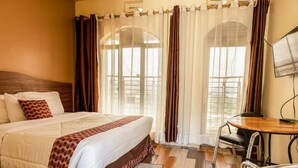 Una camera d'albergo con un letto grande, una scrivania in legno e vista attraverso una finestra con tende.