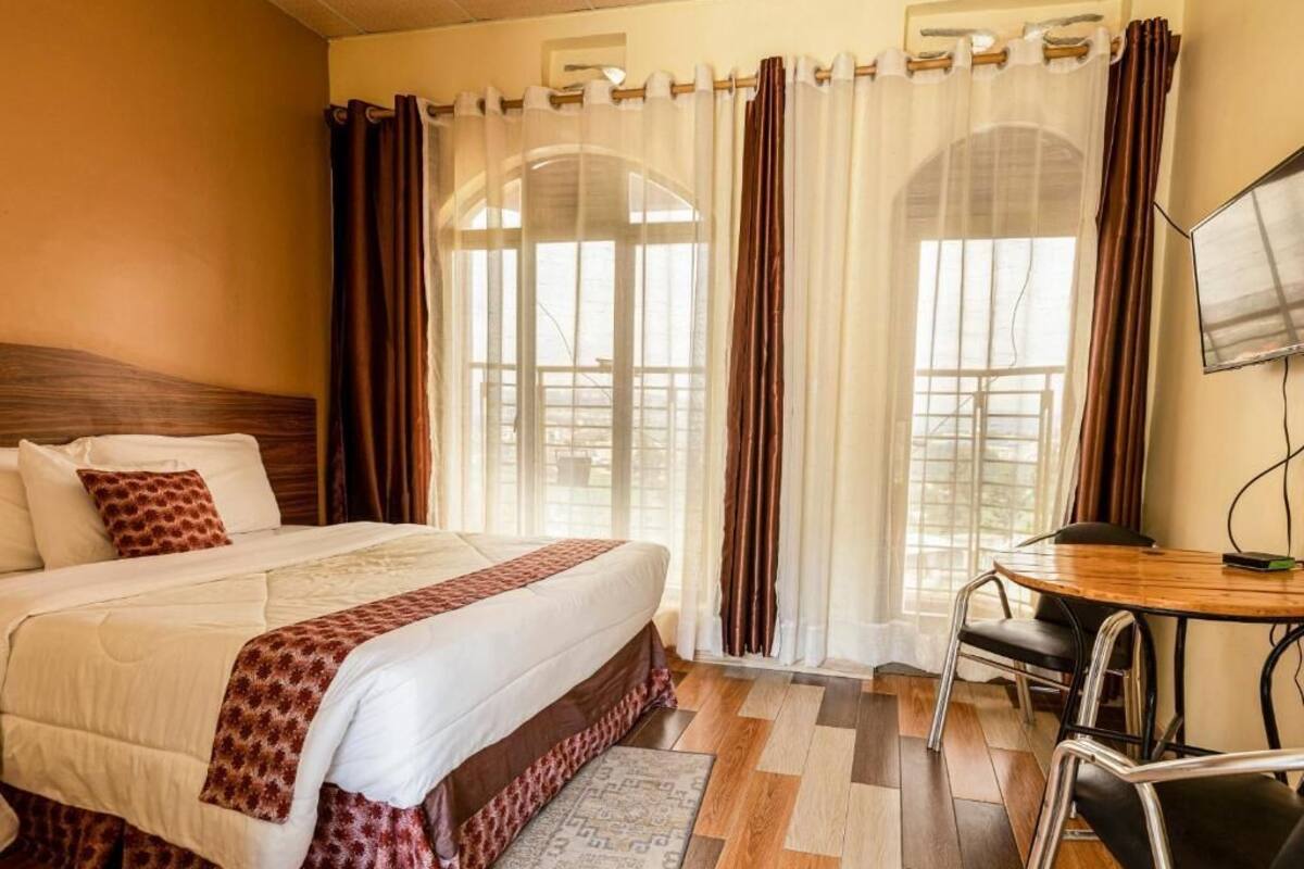 Habitación de hotel con una cama grande, un escritorio de madera y vistas a través de una ventana con cortinas.