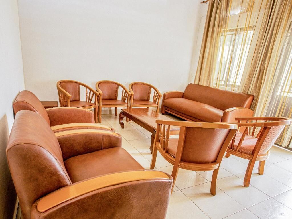A room with a brown leather sofa, two wooden chairs, a wooden coffee table, and a window with curtains.