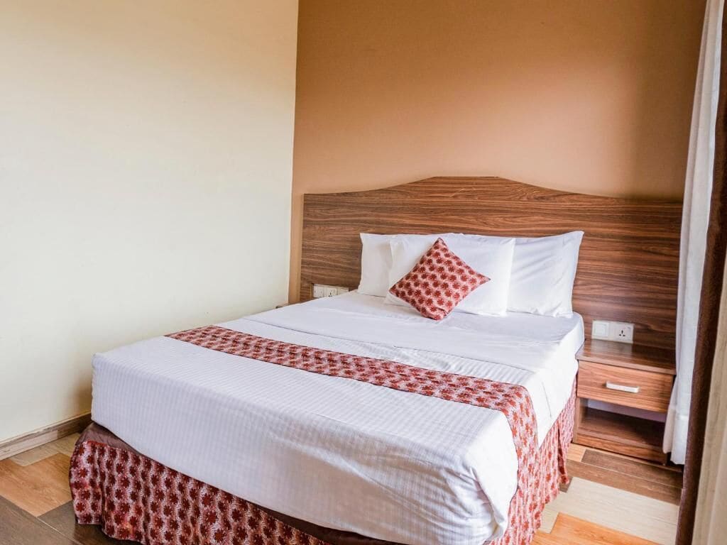 A neatly made bed with a patterned bedspread and pillows, a wooden headboard, and a nightstand with a drawer.