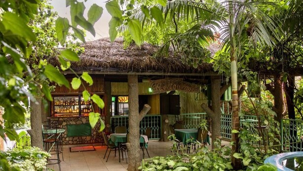 Un ristorante all'aperto con tetto di paglia, immerso nel verde e circondato da una ricca vegetazione.