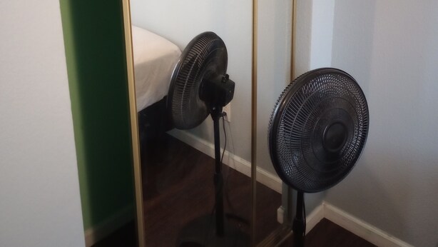 Una habitación pequeña con un armario de puerta corredera, una cama y dos ventiladores de pie.