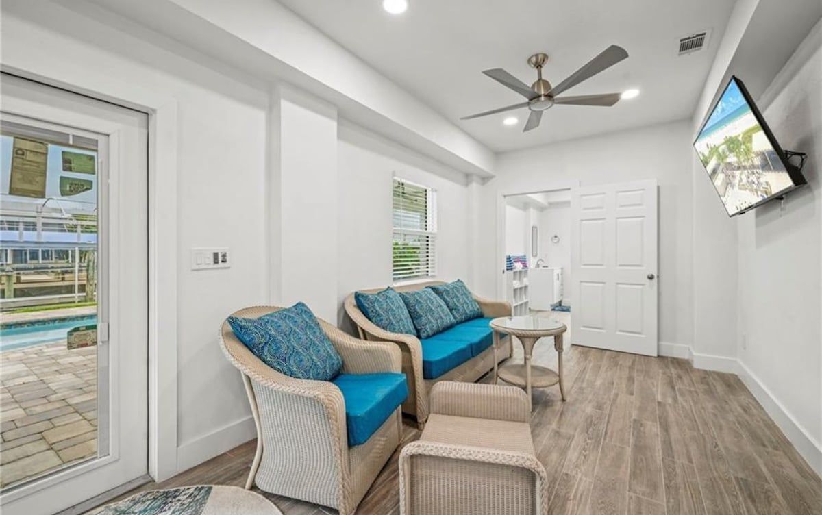 A room with wicker furniture, a ceiling fan, a television, and a view of a pool.