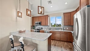 A modern kitchen with wooden cabinets, stainless steel appliances, a marble island, and pendant lighting. - Ibis Landing - Boat Lift & Gulf Access (Fort Myers Beach)